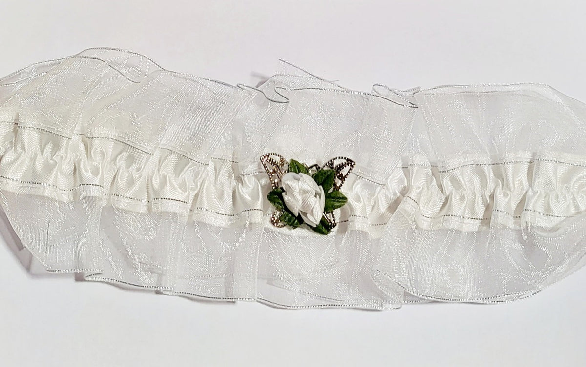 White satin bridal garter with an organza overlay, decorated with a silver filigree butterfly and a white silk rose, photographed as a delicate accessory for brides.