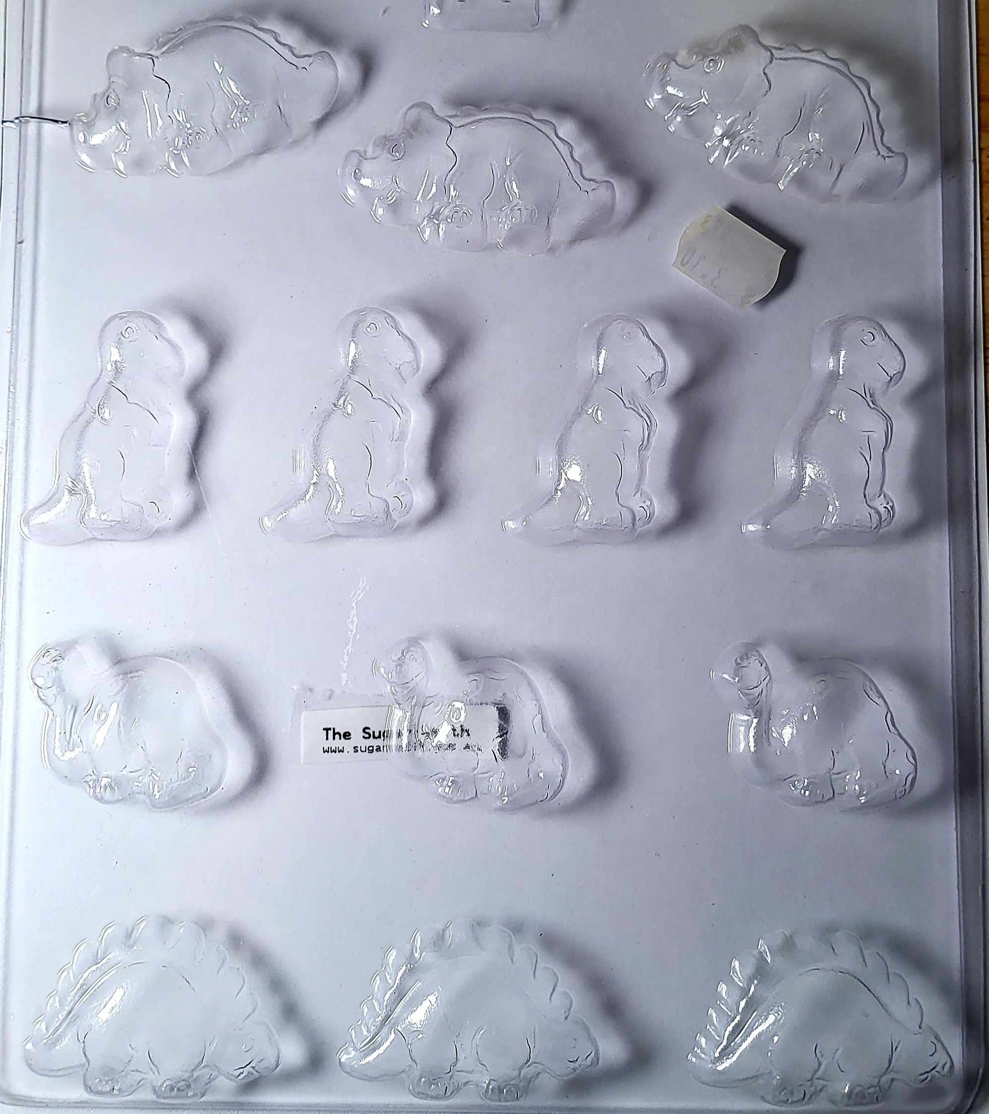 A set of clear plastic dinosaur-shaped chocolate moulds with various dinosaur designs including a triceratops.