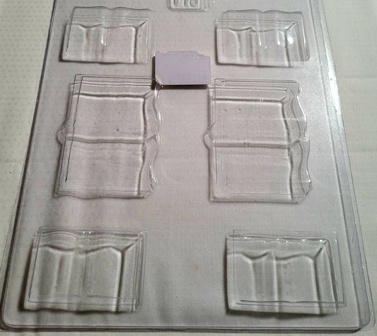 A clear plastic open book-shaped chocolate mould with cavities for various sizes of books.