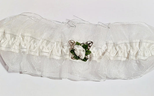 White satin bridal garter with an organza overlay, decorated with a silver filigree butterfly and a white silk rose, photographed as a delicate accessory for brides.