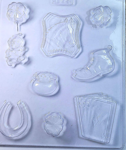 A clear plastic chocolate mould featuring shapes of a three-leaf clover, a horse shoe, a leprechaun, a pot of gold, a horse head with a good luck sign, a lucky boot, and four aces from playing cards.