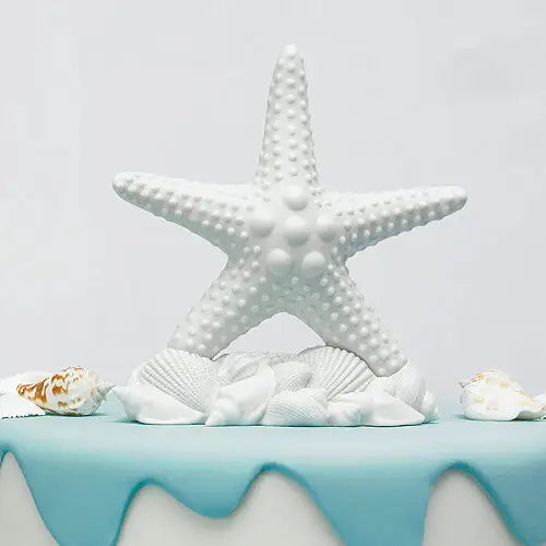 White bisque starfish cake topper with seashell base, suitable for beach‑themed wedding cakes.